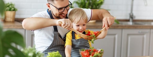 Ein Vater und ein Kind beim gemeinsamen Mischen von Salat in einer Schüssel