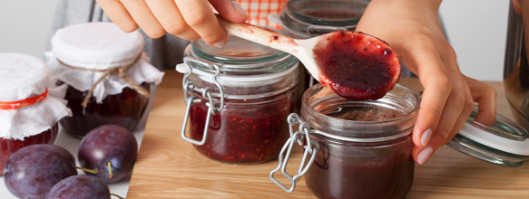 Eine Person beim Abfüllen von frischgekochter Marmelade in ein Einweckglas