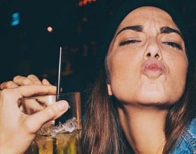 Eine Frau mit einem Glas in der Hand macht einen Kussmund