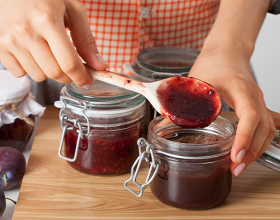 Eine Person beim Abfüllen von frischgekochter Marmelade in ein Einweckglas