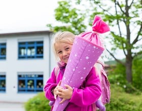 Ein kleines lachendes Mädchen in einer rosa Jacke mit einer Schultüte in den Armen