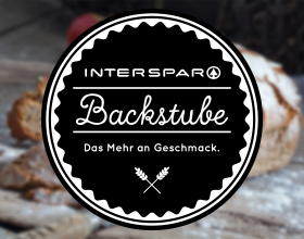 Großes INTERSPAR Backstube-Logo vor einem verschwommenen Brot-Hintergrund 