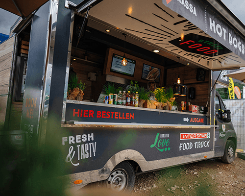 INTERSPAR Foodtruck mit geöffnetem Verkaufsfenster auf einem Schotterplatz