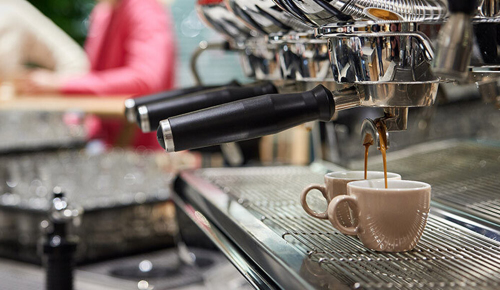Kaffee fließt aus einer Kaffeemaschine in zwei Tassen