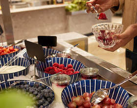Eine Person nimmt sich frische Beeren an einem Müsli-Buffet 