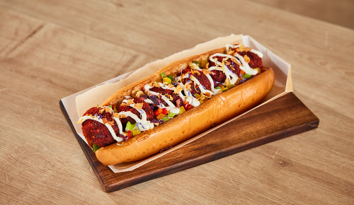 Ein Falafel-Hotdog mit Sauce, Paprikawürfeln und Zwiebeln in einem Brot