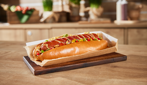 Ein Krainer-Hotdog mit einer Kässekrainer, Relish, Senf und Röstzwiebeln