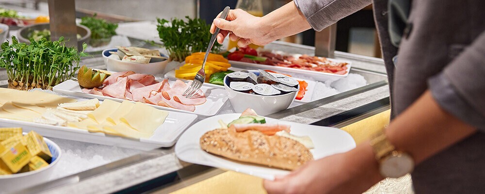 Eine Person nimmt sich eine Scheibe Schinken von einem Buffet
