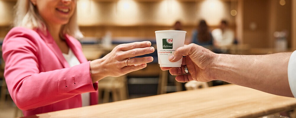 Eine Frau bekommt einen Kaffee zum Mitnehmen gereicht
