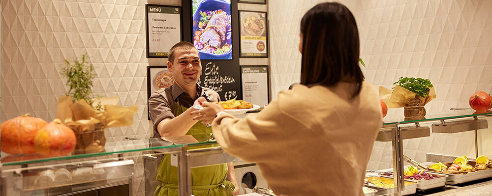 Eine Frau bekommt Essen von einem INTERSPAR-Mitarbeiter gereicht
