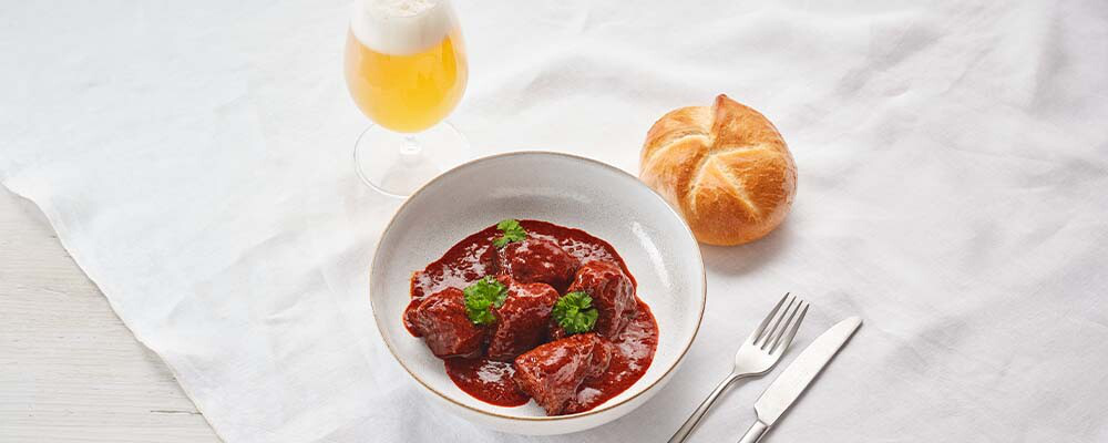 Frisches Rindsgulasch mit einer Semmel und einem Glas Bier