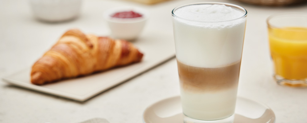 Ein Glas Café Latte und ein Teller mit einem Croissant