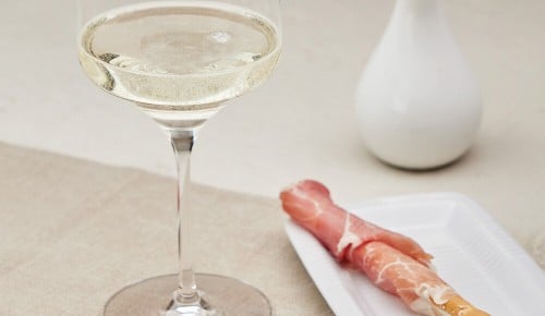 Ein Glas Weißwein und ein Brot-Stick mit Prosciutto