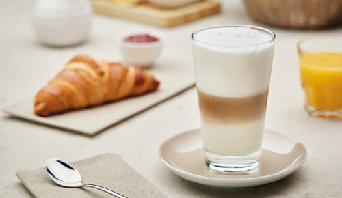 Ein Caffé Latte in einem Glas neben einem Croissant und Glas Orangensaft