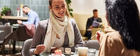 Eine Frau sitzt lächelnd an einem Tisch und isst ein Stück Kuchen
