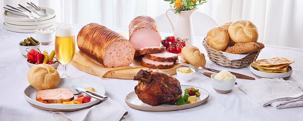 Ein gedeckter Tisch mit herzhaften Speisen aus dem INTERSPAR Partyservice: Leberkäse, Heurigenstelze, Gebäck und Beilagen