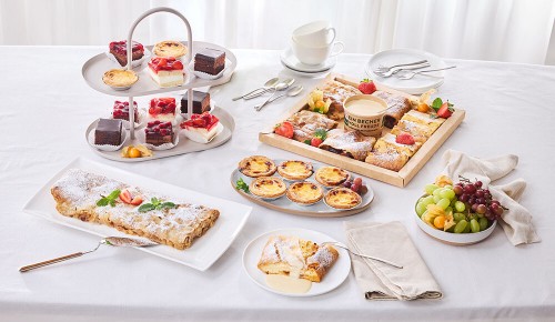 Eine gedeckter Tisch mit verschiedenen Desserts: Apfelstrudel, Pasteis de Nata, Mini-Schnitten