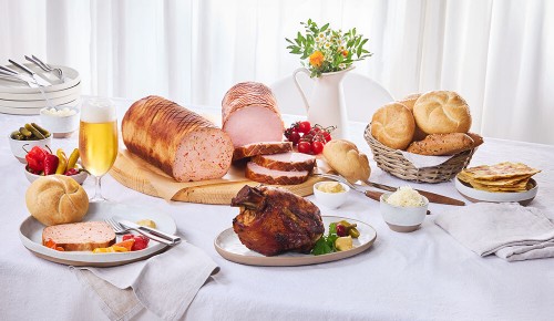 Ein gedeckter Tisch mit herzhaften Speisen aus dem INTERSPAR Partyservice: Leberkäse, Heurigenstelze, Gebäck und Beilagen