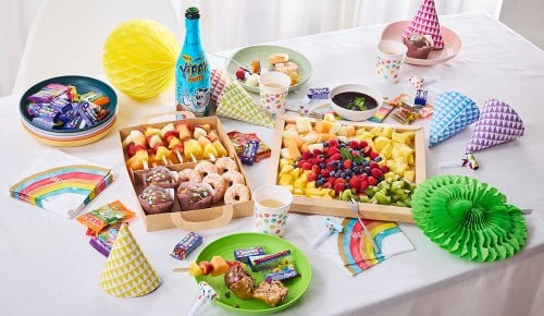 Eine gedeckter Tisch für eine Kinder-Geburtstagsparty mit einer bunten Box voll Donuts, Obst und Co aus dem INTERSPAR-Partyservice