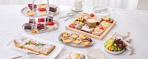 Eine gedeckter Tisch mit verschiedenen Desserts: Apfelstrudel, Pasteis de Nata, Mini-Schnitten