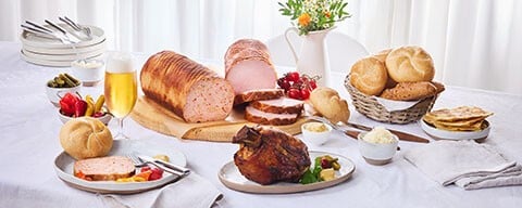 Ein gedeckter Tisch mit herzhaften Speisen aus dem INTERSPAR Partyservice: Leberkäse, Heurigenstelze, Gebäck und Beilagen