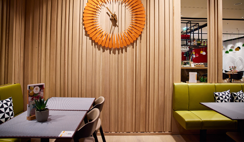 Zwei Tische und eine eine orangene Wanduhr in einem Café Cappuccino