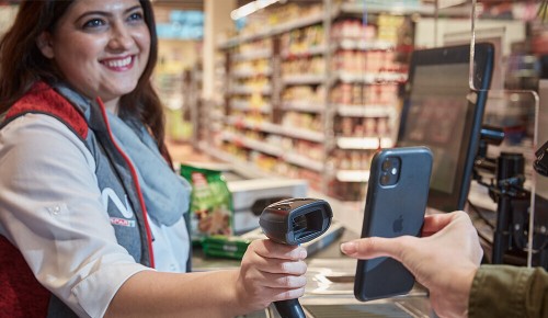Eine Mitarbeiterin scannt ein Handy an einer INTERSPAR-Kassa