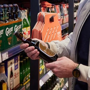 Eine Person steht vor einem Regal und hält eine Bierflasche in der Hand