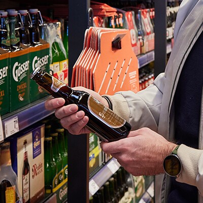 Eine Person steht vor einem Regal und hält eine Bierflasche in der Hand
