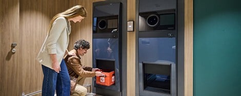 Ein Mann und eine Frau geben einen Getränkekasten in einen Getränkeautomat
