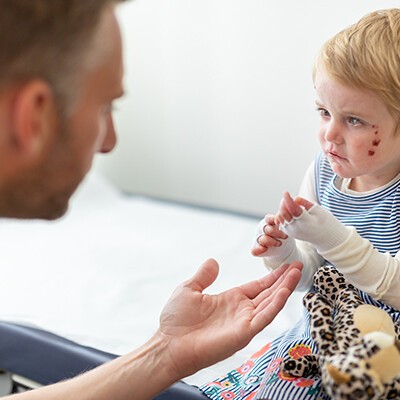 Ein kleines Mädchen mit der EB-Erkrankung sitzt mit verbundenen Händen auf einem Krankenbett