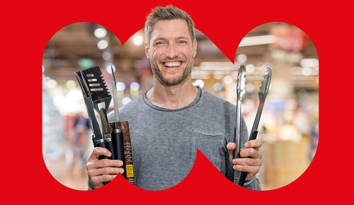 Ein lachender Mann mit den Händen voller Grillzubehör