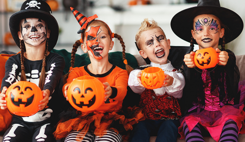 Mehrere, passend zu Halloween verkleidete und geschminkte, Kinder auf einem Sofa