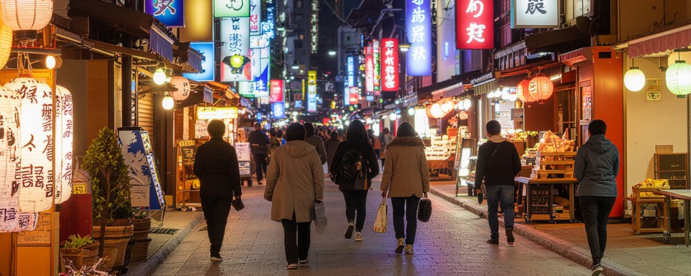 Mehrere Personen spazieren über eine Straße in einer asiatischen Großstadt mit vielen bunten Neonlichtern