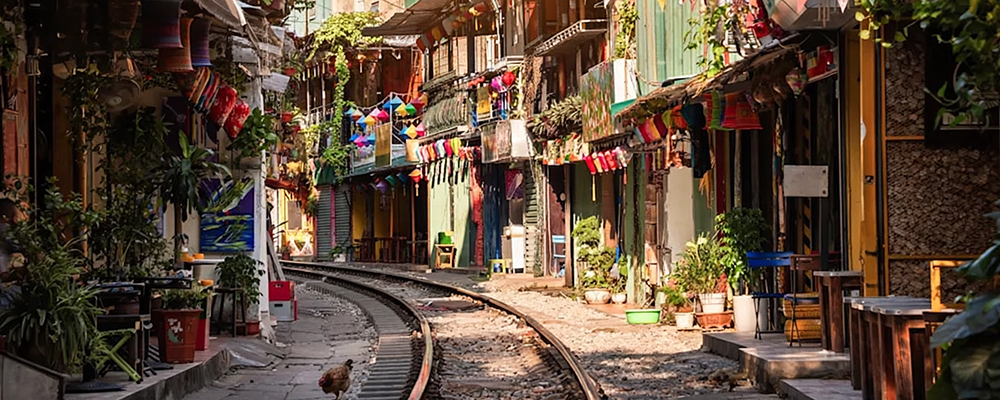 Blick auf eine traditionelle bunte vietnamesische Straße auf dessen Mitte sich Zuggleise befinden