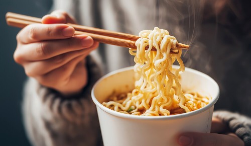 Eine Person isst gerade eine asiatische Nudelsuppe mit Essstäbchen aus einem Becher