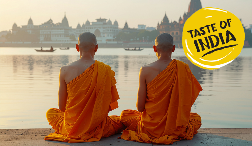 Zwei buddhistische Mönche sitzen am Ufer eines indischen Flusses mit einer Stadt im Hintergrund