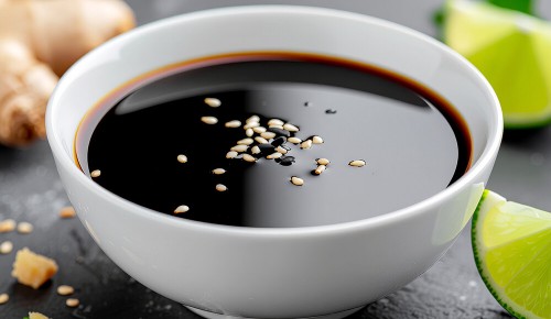 Ein weißes Schälchen gefüllt mit einer glänzenden Sauce bestehend aus Sojasauce, Sesam, Ingwer und Limette