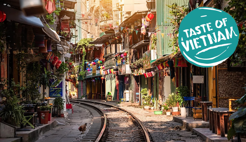 Blick auf eine traditionelle bunte vietnamesische Straße auf dessen Mitte sich Zuggleise befinden