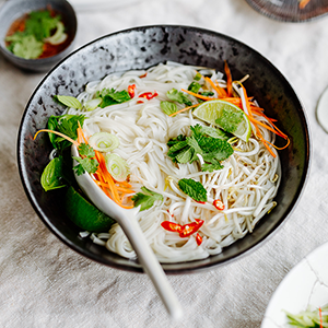 SPAR Mahlzeit Pho Suppe mit einem weißen Suppenlöffel in einem dunklen Teller