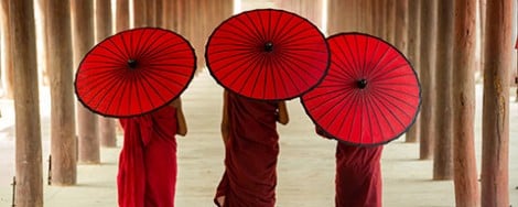 Buddhistische Priester in roten Gewändern mit roten Sonnenschirmen