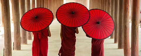 Buddhistische Priester in roten Gewändern mit roten Sonnenschirmen