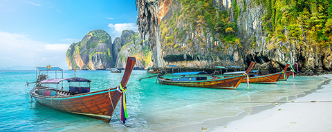 Zwei traditionelle thailändische Boote im türkisen Wasser an einem Sandstrand