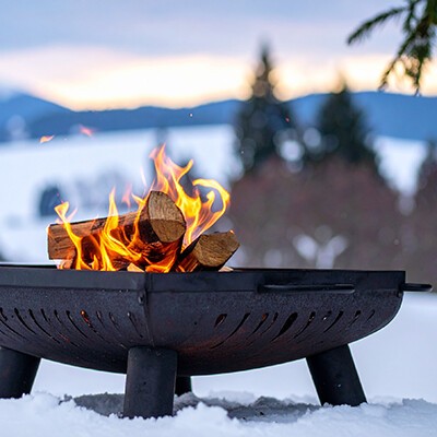 Eine eiserne Feuerschale mit brennenden Holzscheiten im Schnee