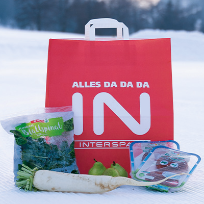 Eine INTERSPAR-Einkaufstasche mit verschiedenen Lebensmitteln im Schnee