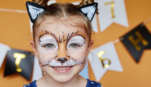 Ein kleines Mädchen mit einer Katzen-Gesichtsbemalung und Ohren an einem Haarreif