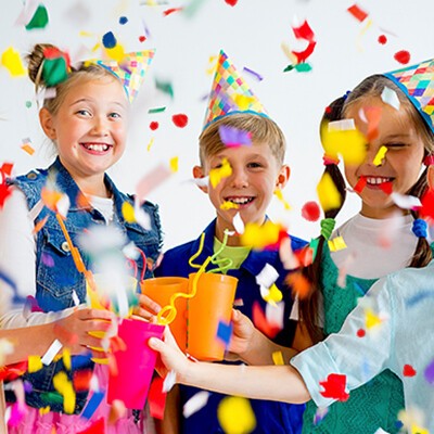 Mehre Kinder mit Partyhüten und fliegendem Konfetti beim Feiern
