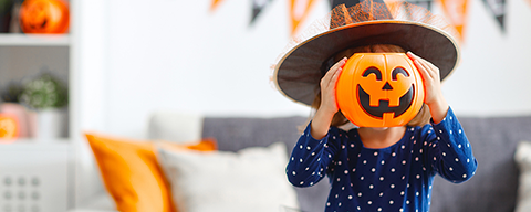 Ein kleines Mädchen in einem Hexenkostüm hält einen Halloweenkürbis vor ihr Gesicht
