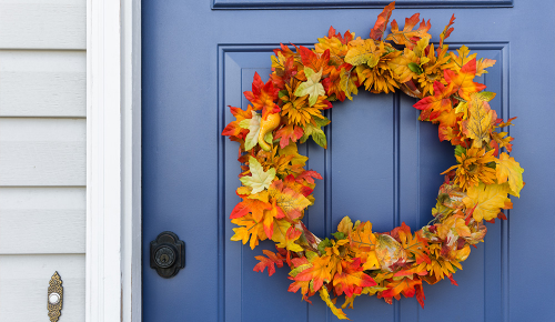Ein runder Kranz aus Herbstblättern an einer blauen Haustüre