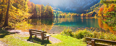 Eine Holzbank im Sonnenschein an einem Bergsee